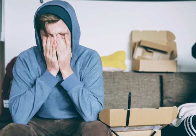 Person, scheinbar müde, sitzt mit den Händen über dem Gesicht