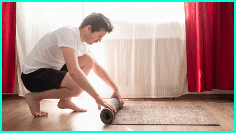 Mann rollt eine Yogamatte aus