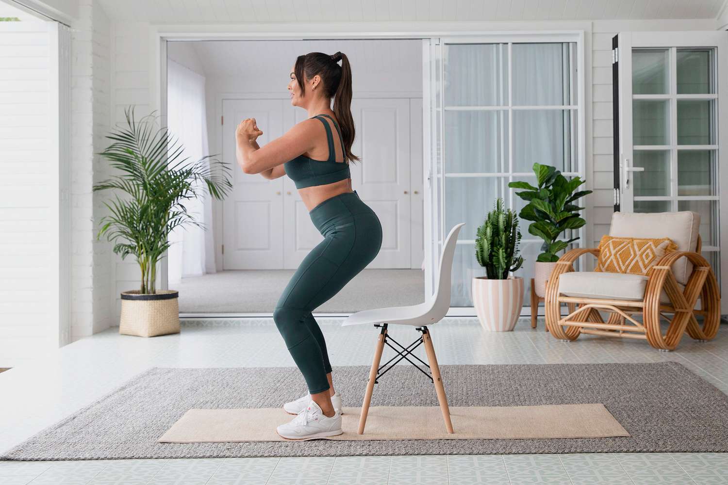 Frau im grünen Trainingssatz, der über weißem Stuhl hockt